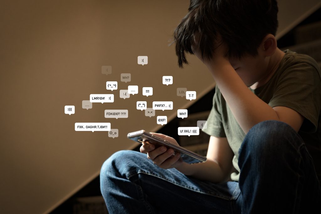 cyberbullying social media harassment concept. young asian preteen, teenager boy looking at his smartphone feeling frustrated after reading bad comments. text emoticons. bully, teen mental health